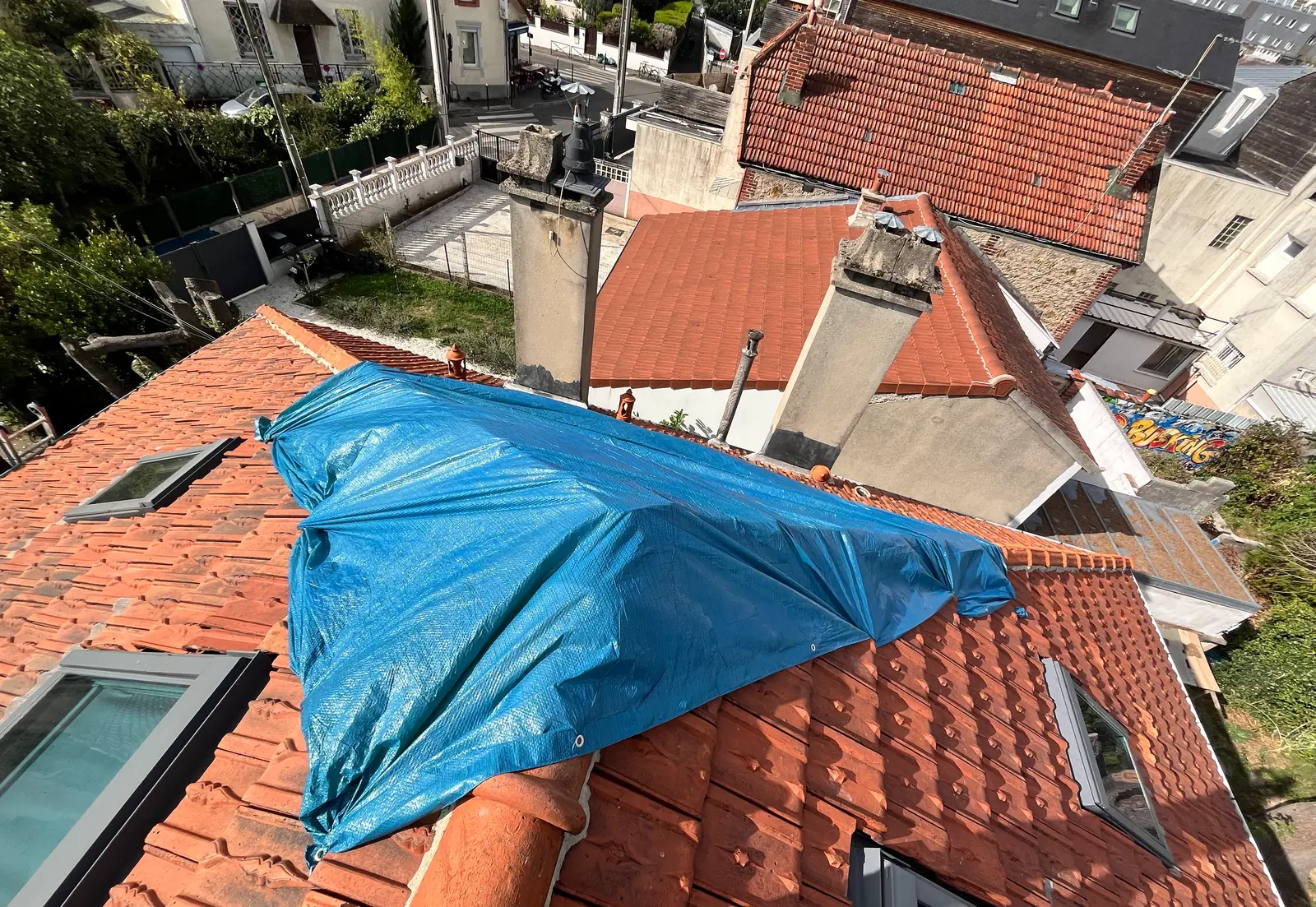 Bâche bleue tendue sur une toiture en tuiles à Villejuif après l'orage de grêle, entre les cheminées